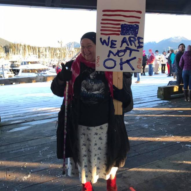 Old woman holding upside US flag sign during anti-orange fascist march, 2017.